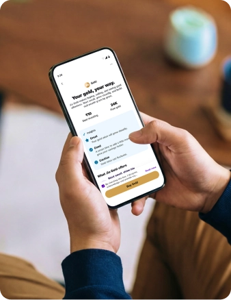 Person holding a mobile device to invest in digital gold, displaying a user interface for 24K pure gold starting at ten rupees with market insights.